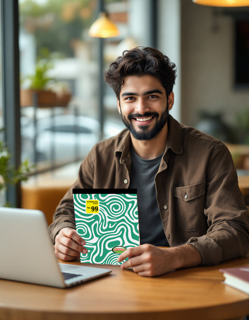 Man holding a Srinivasa notepad , sitting at a table with a laptop.